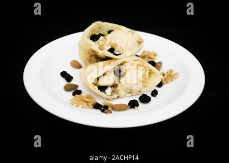 Pita pocket pane farcito con caramello gelato, noci, mandorle e uvetta (essiccato di uva nera), pronto a mangiare, su sfondo nero Foto Stock