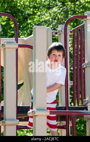 Little Boy giocando sul parco giochi presso il parco della città in una calda giornata estiva. Foto Stock