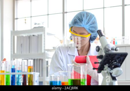 La scienziata nel laboratorio di fare esperimenti con liquido chimico e facendo e lista di controllo per registrare i dati dei test in laboratorio. Foto Stock
