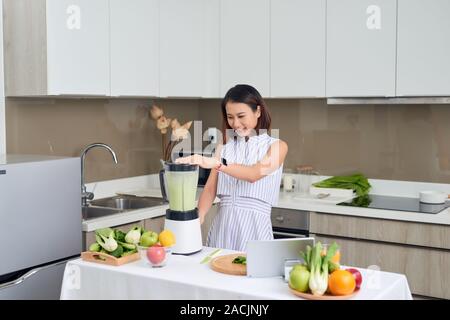 Bella donna asiatica a spremere il succo facendo succo verde con succo macchina nella cucina di casa. Un sano concetto. Foto Stock