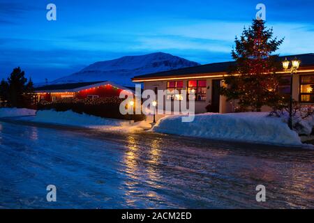 Tipiche Case islandese con decorazioni di Natale al crepuscolo vicino a Akureyri, il nord dell'Islanda. Strada sdrucciolevole in primo piano. Foto Stock