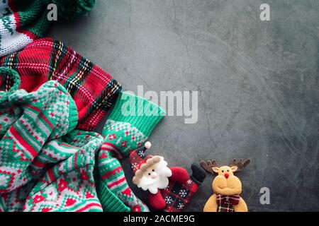 Maglione verde e rosso scotch blanket posa su cemento sfondo con una Santa Claus bambola e una renna per ornamento di Natale con spazio di copia Foto Stock