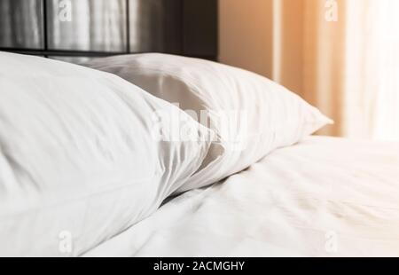 Cuscini bianchi i laici a un letto vuoto vicino alla finestra con la luce del mattino, foto di sfondo con il fuoco selettivo Foto Stock