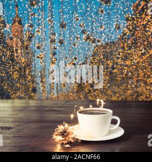 Tazza di caffè nero sulla tavola di legno al cafe'. Sfocata ghirlanda dorata in città come sfondo. Vacanze di Natale in tempo. Foto Stock