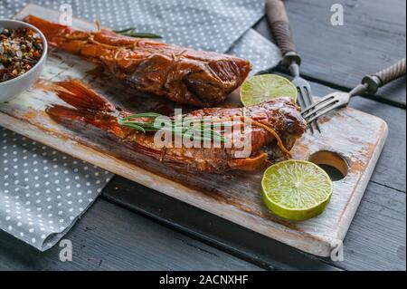 Close-up hot pesce affumicato su un tagliere di legno. Rosso filetto di branzino. Foto Stock