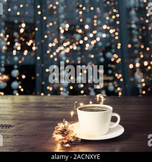 Tazza di caffè nero sulla tavola di legno al cafe'. Sfocata ghirlanda dorata in città come sfondo. Luci della Citta'. Vacanze di Natale in tempo. Foto Stock