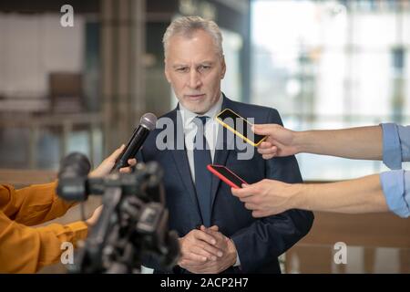 Grigio-dai capelli uomo barbuto avente un discorso alla conferenza stampa Foto Stock