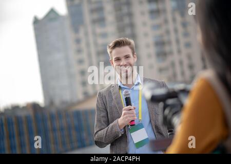 Giovani reporter barbuto tenendo un microfono in mano Foto Stock