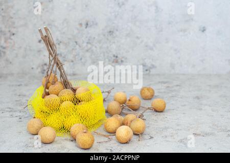 Longan esotica frutta in una sacca di stringa su sfondo grigio. Posto per il testo. Close-up. Copia dello spazio. Vista dall'alto. Foto Stock