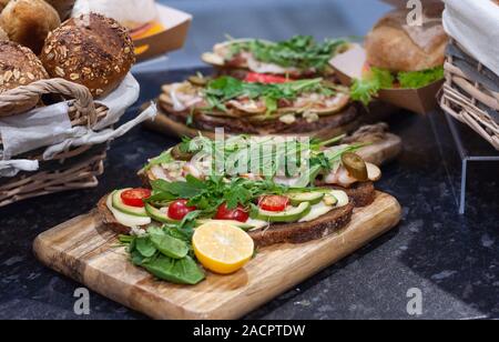 Panini con pomodori, lattuga, prosciutto, succo di limone e foglie di rucola sul pane scuro. Foto Stock