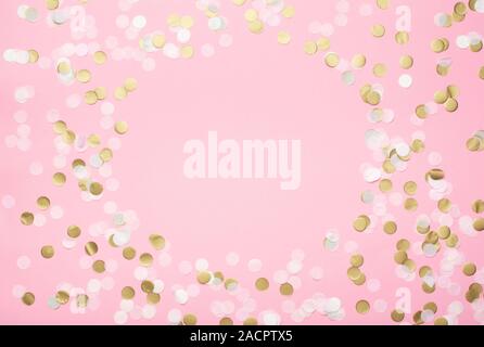 Coriandoli di carta in rosa chiaro, bianco e oro pastello su sfondo rosa, vista dall'alto, selettivo Foto Stock