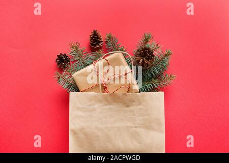 Carta di Natale borsa con regali e decorazioni naturali per rifiuti zero vacanza sul rosso. Xmas Shopping eco concetto. Vista da sopra, piatto laici. Foto Stock
