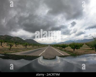 Pov guida un auto nera su due strada asfaltata con viste sulla campagna in Murcia con sparse nere nuvole basse. A guidare attraverso una terra spagnola con mou Foto Stock