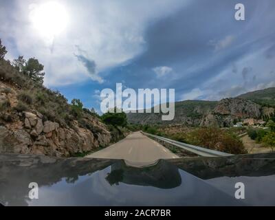 POV alla guida di una vettura su una solitaria a due vie per strada di montagna con vista di alcuni alberi della campagna di Murcia con un sacco di nuvole. Guidando attraverso il mounta Foto Stock