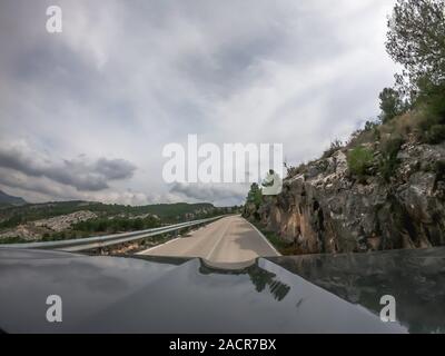 POV alla guida di una vettura su una solitaria a due vie per strada di montagna con vista di alcuni alberi della campagna di Murcia con un sacco di nuvole. Guidando attraverso il mounta Foto Stock