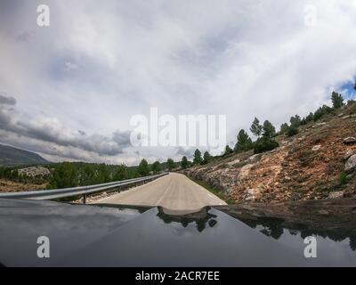 POV alla guida di una vettura su una solitaria a due vie per strada di montagna con vista di alcuni alberi della campagna di Murcia con un sacco di nuvole. Guidando attraverso il mounta Foto Stock