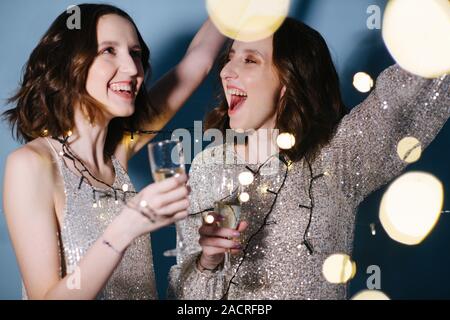 Gemelle in lucenti abiti da sera celebrare con bicchieri di vino spumante Foto Stock