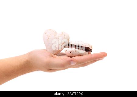 Mano trattiene forma di cuore le meringhe al cioccolato. Foto Stock