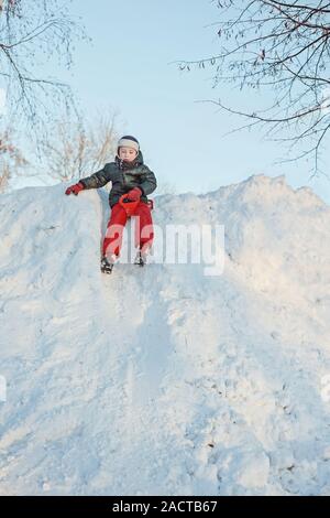 Ragazzo su una slitta di plastica andando giù per una collina nevoso Foto Stock