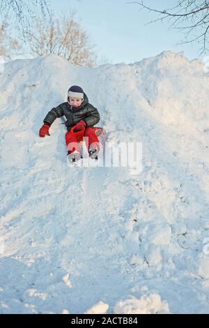 Ragazzo su una slitta di plastica andando giù per una collina nevoso Foto Stock