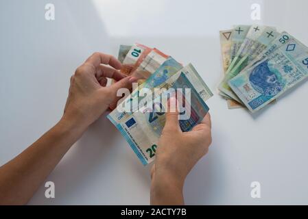 Donna che mantiene Polski Polish Zloty PLN e le banconote in euro in mani. Euro denaro e Polski Polish Zloty PLN in un womans mani su uno sfondo bianco. Di euro in Polonia. Foto Stock