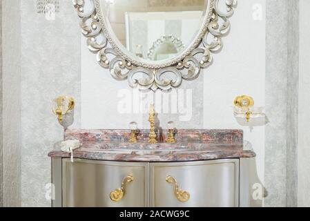 Interno in bagno, specchio vintage e costosi lavabo in marmo, acciaio inox vasca, con maniglie oro close-up. Foto Stock