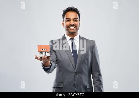 Attività immobiliari e concetto di persone - uomo agente immobiliare con modello di casa su sfondo grigio Foto Stock