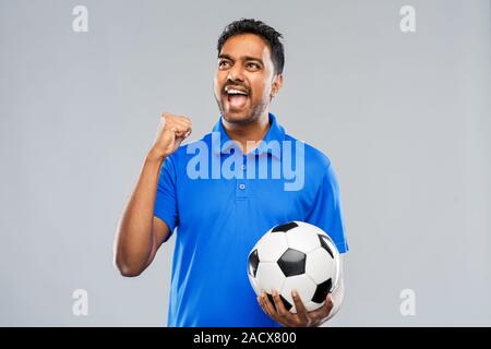 Sport e tempo libero giochi e concetto di successo - happy indian man o appassionato di calcio con pallone da calcio per celebrare la vittoria su sfondo grigio Foto Stock