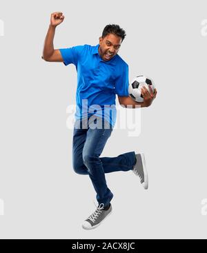 Sport e tempo libero giochi e concetto di persone - happy indian man o appassionato di calcio con pallone da calcio saltando su sfondo grigio Foto Stock