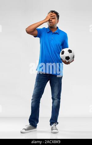 Sport e tempo libero giochi e concetto di errore - deluso uomo indiano o tifoso di calcio con palla su sfondo grigio Foto Stock