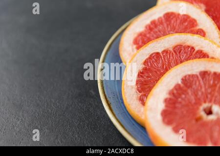 Cibo, frutta e mangiare sano concetto - close up di carni succose fette di pompelmi sulla piastra su sfondo di ardesia Foto Stock