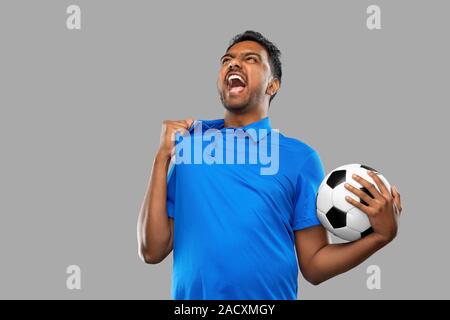 Sport e tempo libero giochi e concetto di successo - emotiva uomo indiano o tifoso di calcio con palla su sfondo grigio Foto Stock