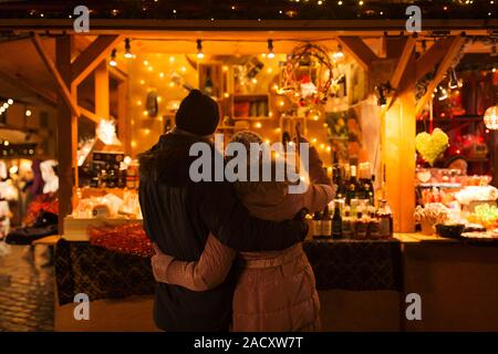 Amore, vacanze invernali e concetto di persone - felice coppia senior avvolgente al mercato di Natale souvenir shop stallo nella sera Foto Stock