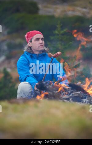 Escursionismo uomo preparare gustose salsicce sul fuoco Foto Stock