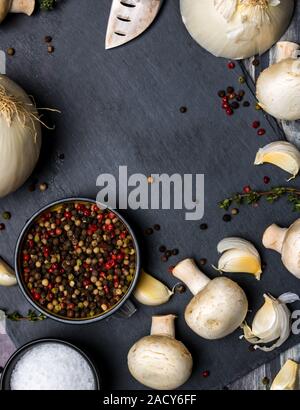 Una vista dall'alto in basso di un nero ardesia tagliere con corso di sale e pepe e aglio e cipolla e funghi con copia spazio in mezzo. Preparazione alimentare co Foto Stock
