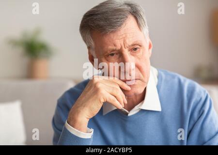 Ritratto di premuto Senior Gentleman seduto sul divano di casa Foto Stock