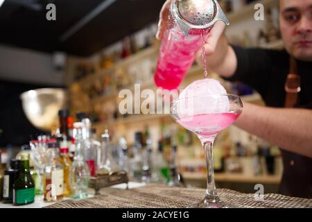 Close-up di barman versa manualmente rosa cocktail drink nel bar Foto Stock