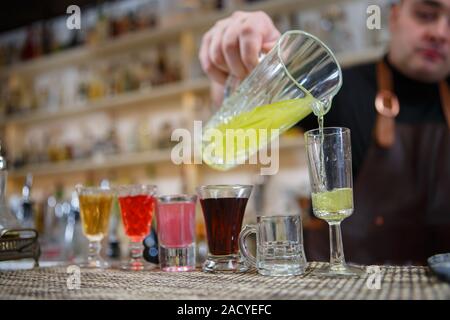 Il barista versa vari di bere alcol in piccoli bicchieri in bar Foto Stock