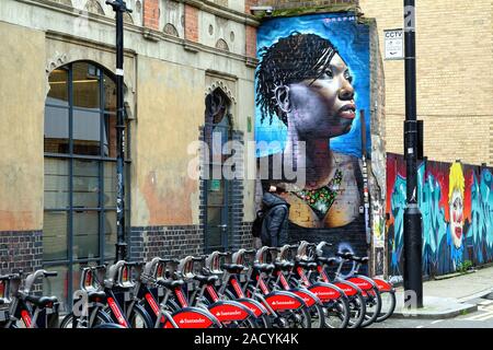 Un unico maschio passato a piedi una spettacolare pezzo di illustrazione di una donna viene spruzzato su una parete in Fashion Street Whitechapel Est Londra Inghilterra REGNO UNITO Foto Stock