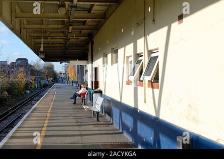 Una donna di mezza età seduta da sola su un vuoto che la stazione ferroviaria piattaforma in attesa di un treno stazione di Kingston Greater London Surrey in Inghilterra REGNO UNITO Foto Stock