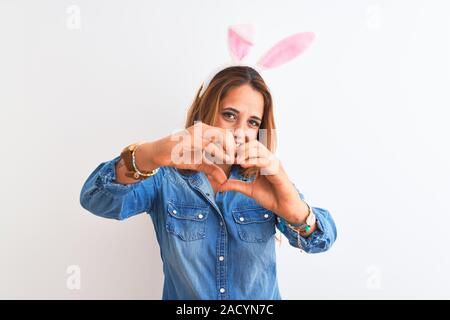 Giovani redhead donna che indossa easter bunny orecchie su sfondo isolato sorridente in amore che mostra il simbolo del cuore e la forma con le mani. Concetto romantico. Foto Stock