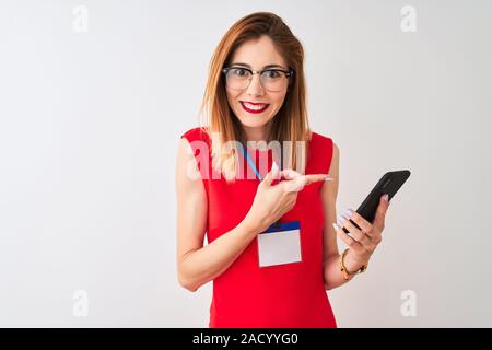 Redhead imprenditrice indossando id card utilizzando lo smartphone isolato su sfondo bianco molto felice puntando con mani e dita Foto Stock