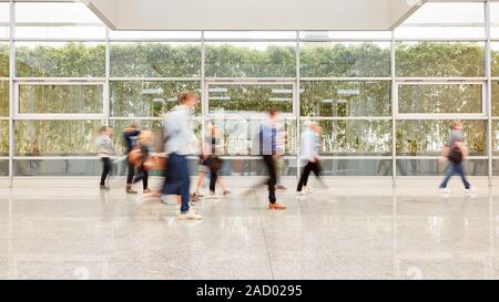 Sfocato persone anonime stanno camminando attraverso una luminosa hall ad una fiera commerciale Foto Stock