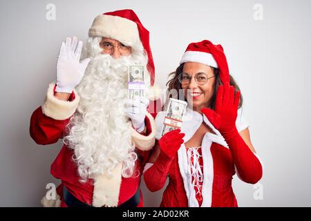 Coppia senior indossando Santa Claus costume holding dollari isolato su sfondo bianco rinuncia a dire ciao felice e sorridente e cordiale benvenuto gest Foto Stock