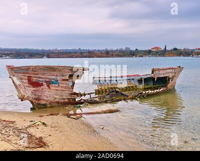 Naufragio di una barca sulla spiaggia sabbiosa di inverno, sotto il cielo nuvoloso. Foto Stock