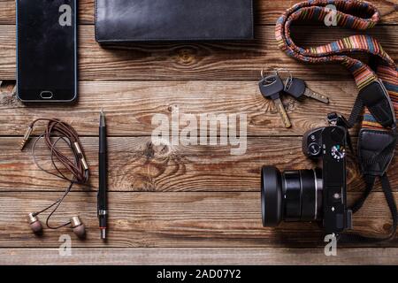 Concetto di viaggio - cuffie, macchina fotografica, taccuino, portamonete, matita e tasti su sfondo di legno. Foto Stock