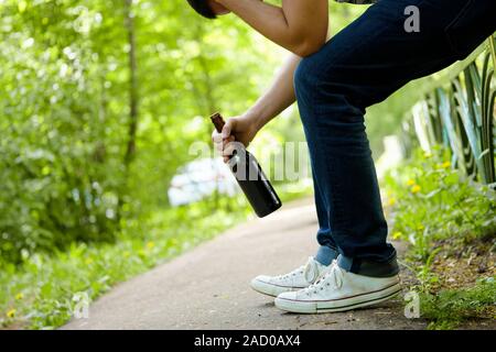 L'uomo premuto con bottiglia di birra seduti sul recinto verde all'aperto. Foto Stock