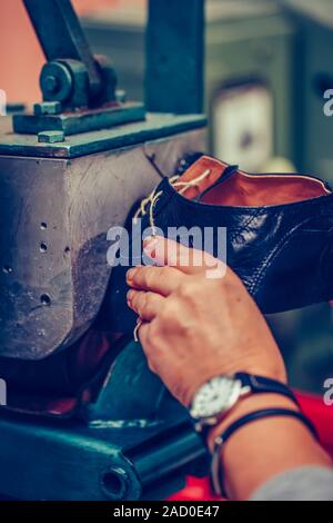 Le mani di un calzolaio esperto utilizzando una speciale macchina utensile per la realizzazione di calzature. Pattino del processo di produzione in fabbrica.Il fuoco selettivo Foto Stock