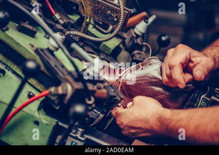 Le mani di un calzolaio esperto usando una speciale macchina per mettere le scarpe sullo stampo, nelle calzature artigianali industria. Messa a fuoco selettiva. Foto Stock