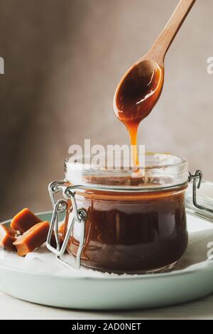 Vaso di vetro con caramello salato e caramelle su sfondo di legno, lo spazio per il testo Foto Stock